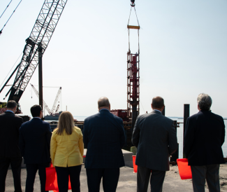 Gov McKee and others standing together looking a construction cranes